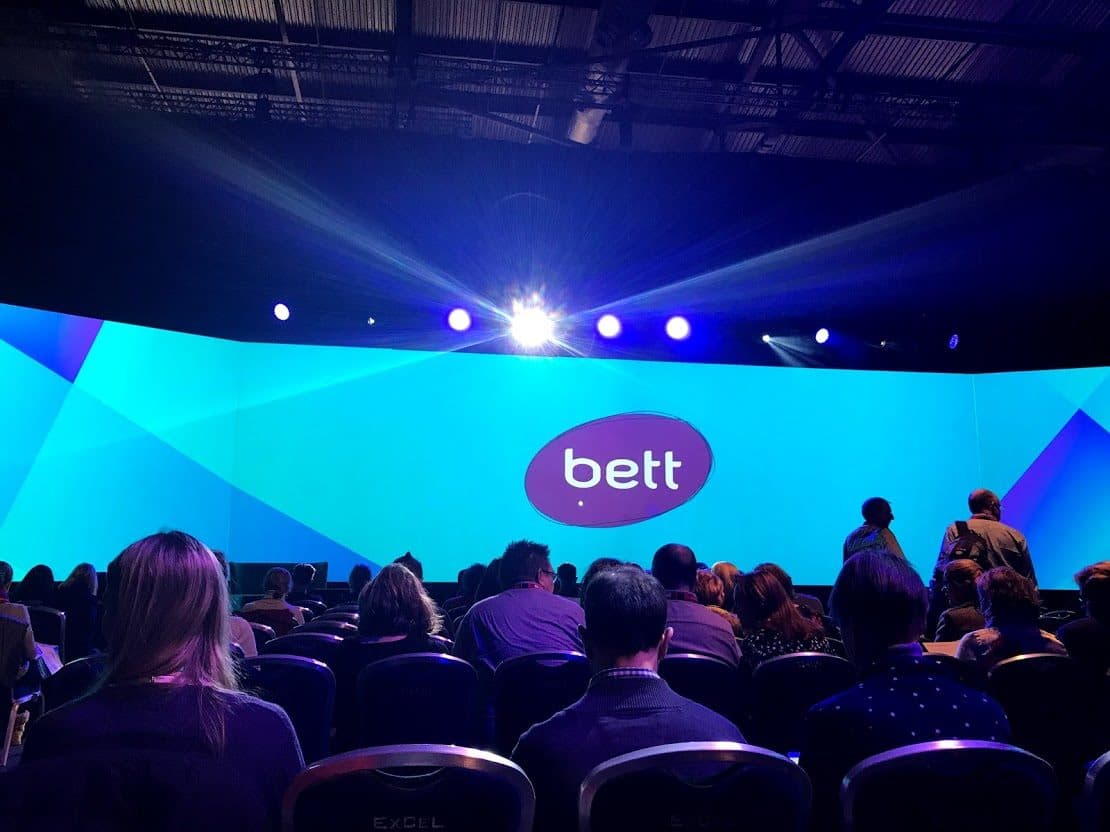 An auditorium with a scattering of people and BETT's logo in the middle of the screen.