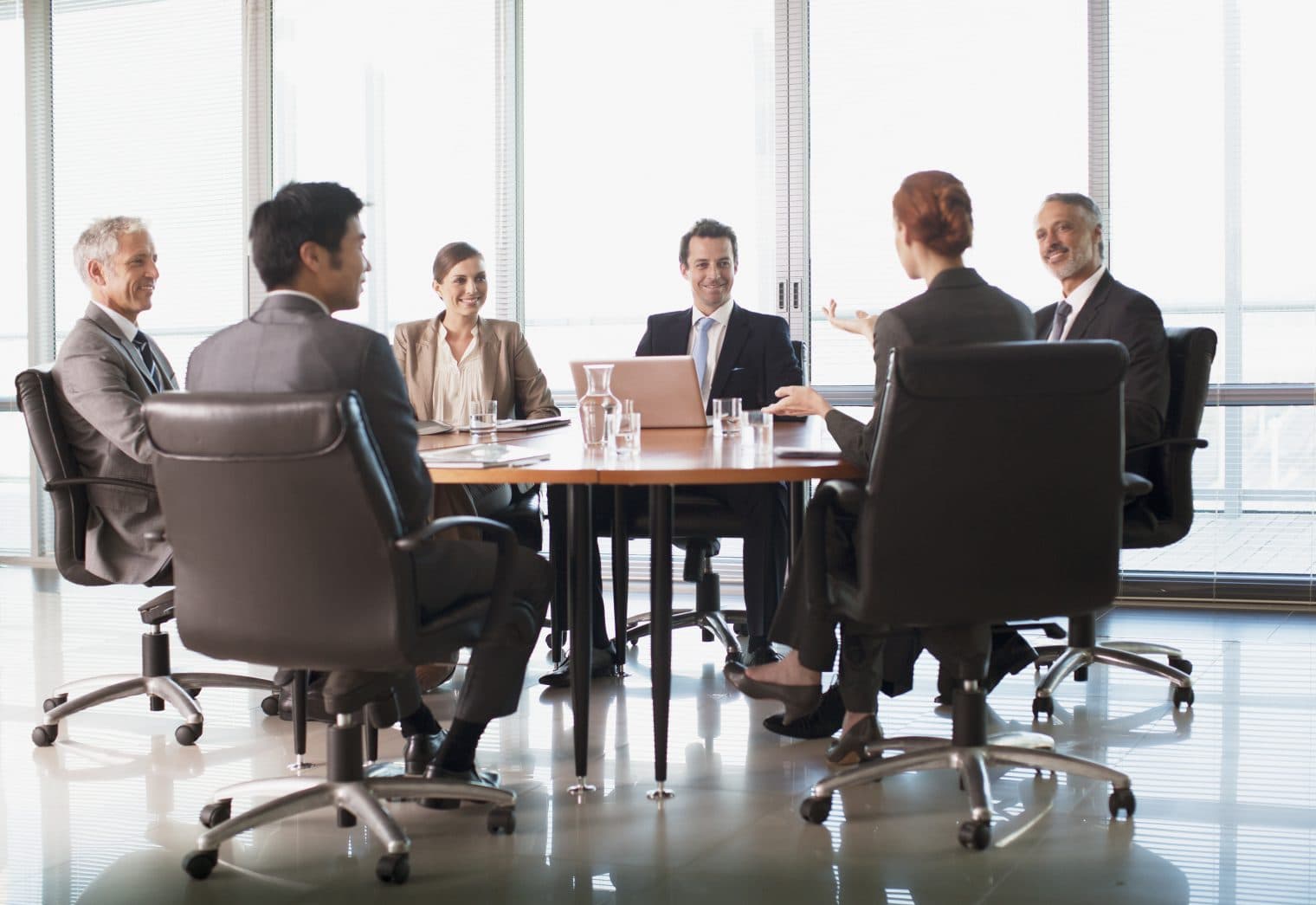 A group of business professionals sat a meeting table in a conference room with glass walls.