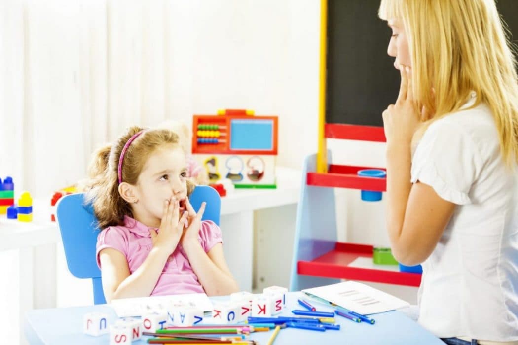 Young girl sat in a chair copies female therapist to sound out a word.