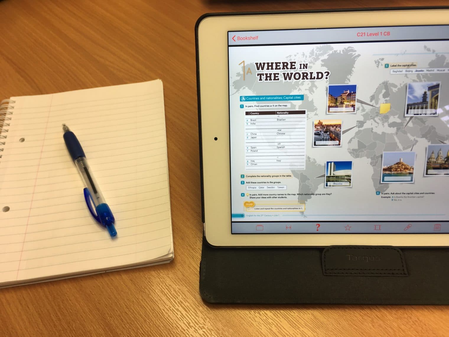An iPad with the first page of C21, level 1 up - the header 'Where in the world?' can be read. A notepad and pen is next to the iPad.