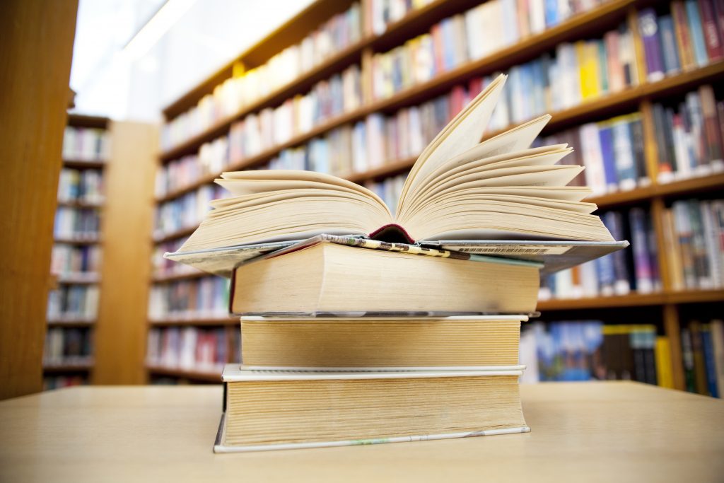 A stack of books in a library, with the top book open in the middle.