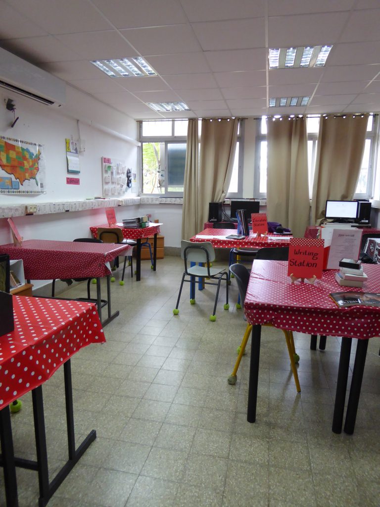 A classroom showing a writing station and literature station on different tables. The chairs have tennis balls on the feet so that there is less noise distraction when the classroom is in use.