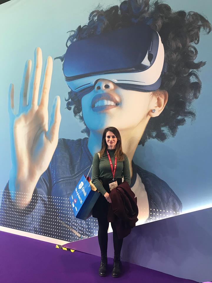 A picture of Ella in front of a large wall mural of a woman wearing a VR headset.