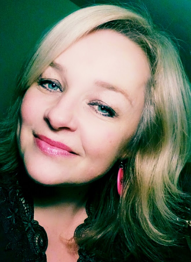 Selfie of Hana, a smiling woman with blonde hair, pink dangling earrings, and a black shirt. 