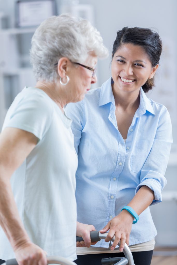 A friendly young woman assisting an elderly woman learning walking with a walking frame.