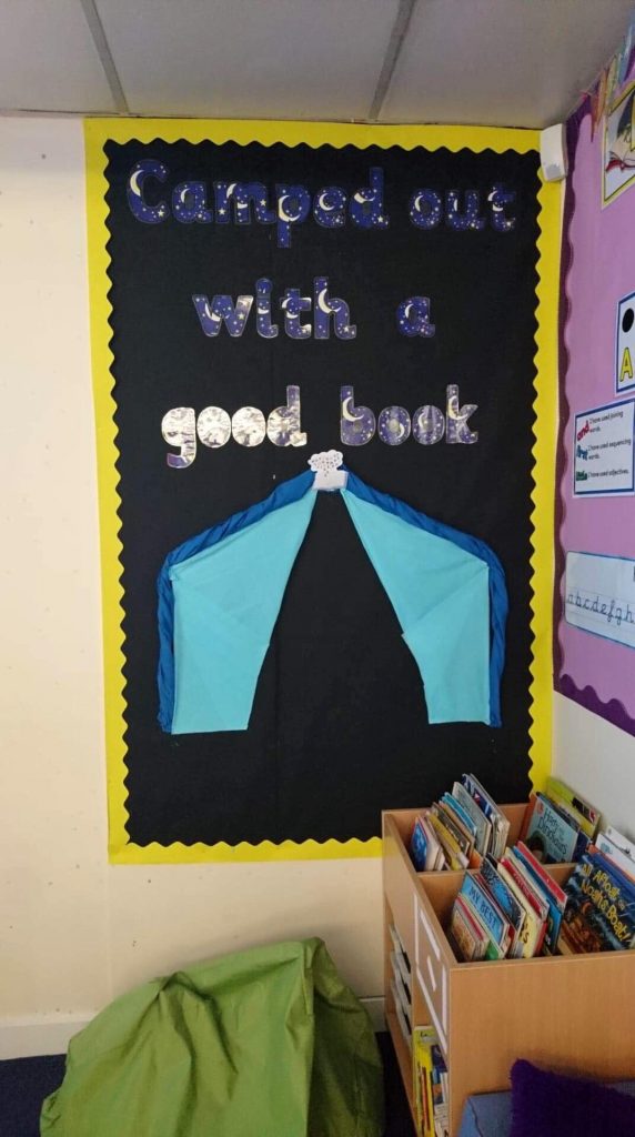 The classroom library, with a colourful display board that has a paper crafted tent, and the sign 'Camped out with a good book'. 