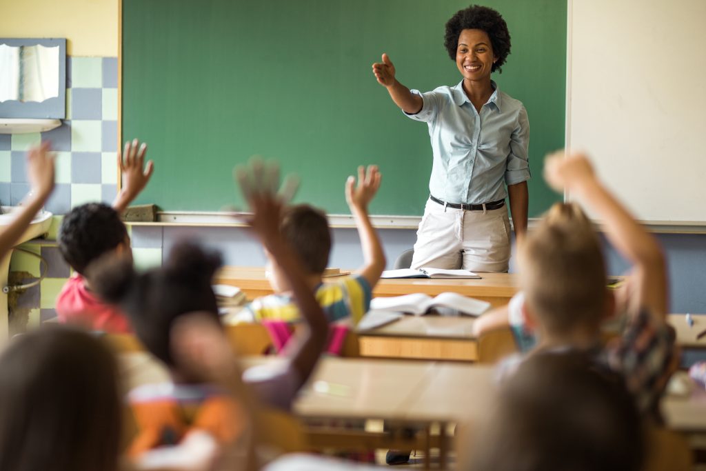 Happy black teacher pointing at a school child to answer her question on a class at elementary school.